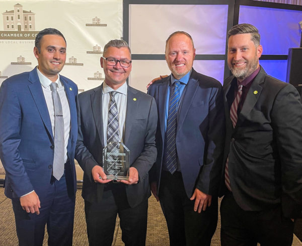 Jurgen Koehler, Chris Gerrits, and Aaron Wignall standing with Nick Mocan while he receives his award